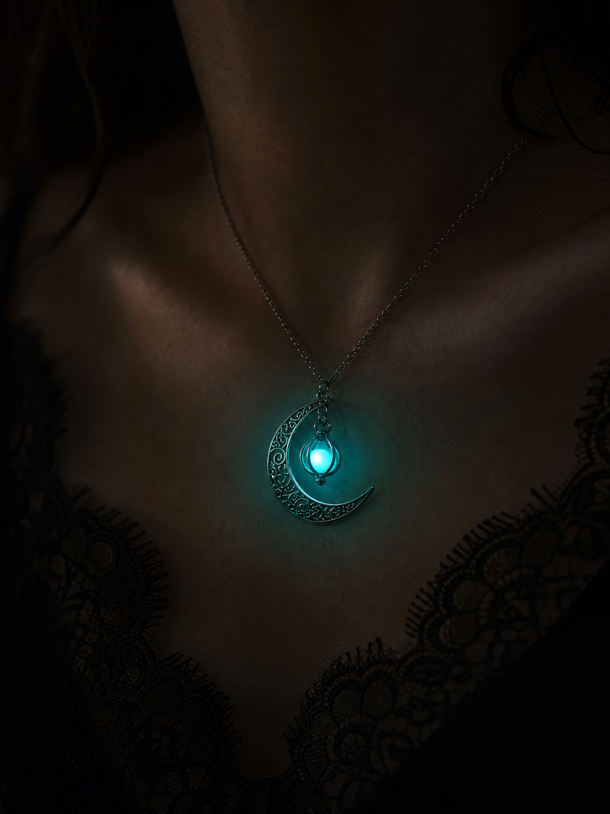 Model wearing the Moonfire glowing crescent moon pendant with luminous teal stone in darkness