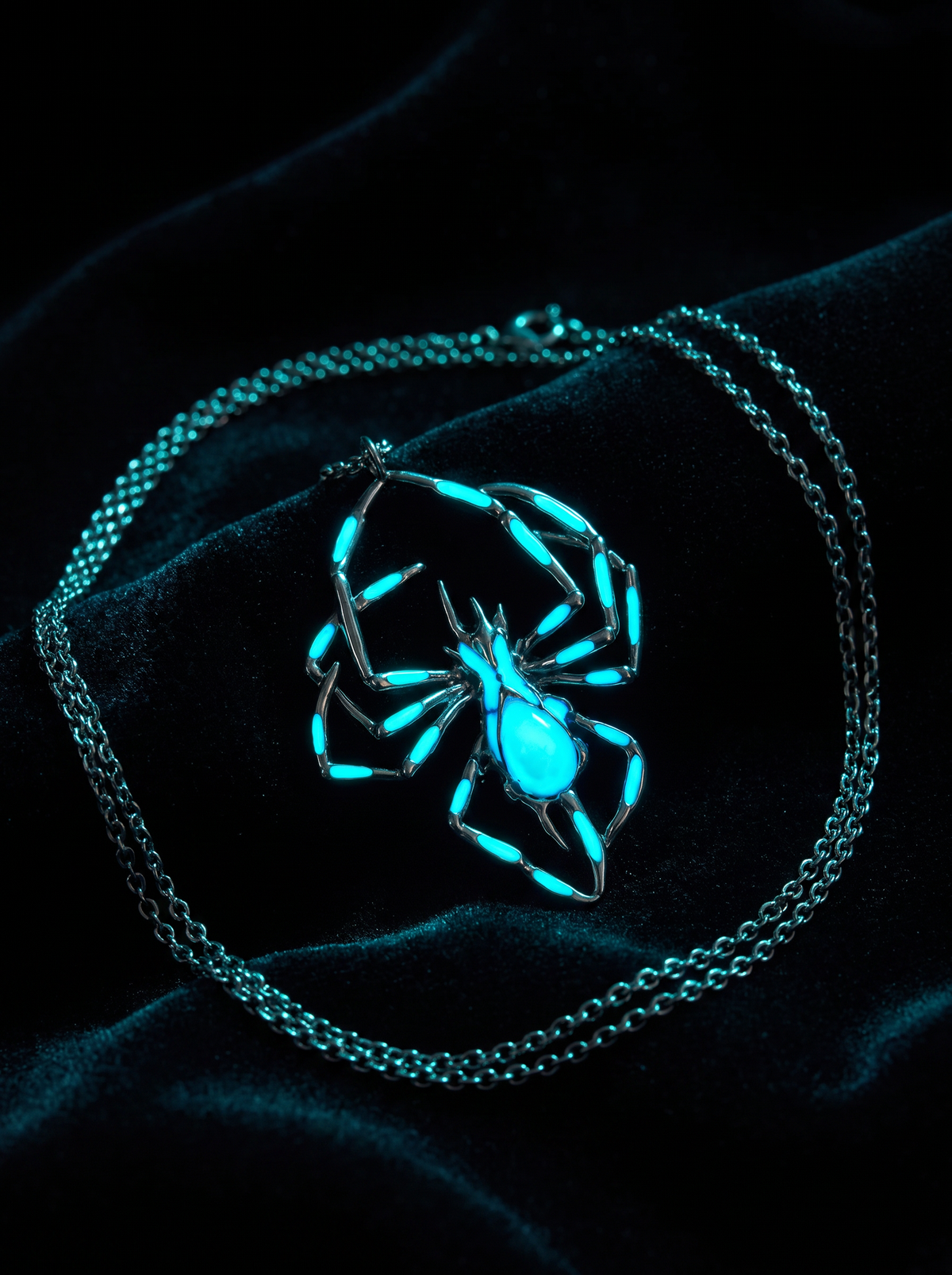 Widow's Glow spider necklace glowing vivid cyan on black velvet in the dark